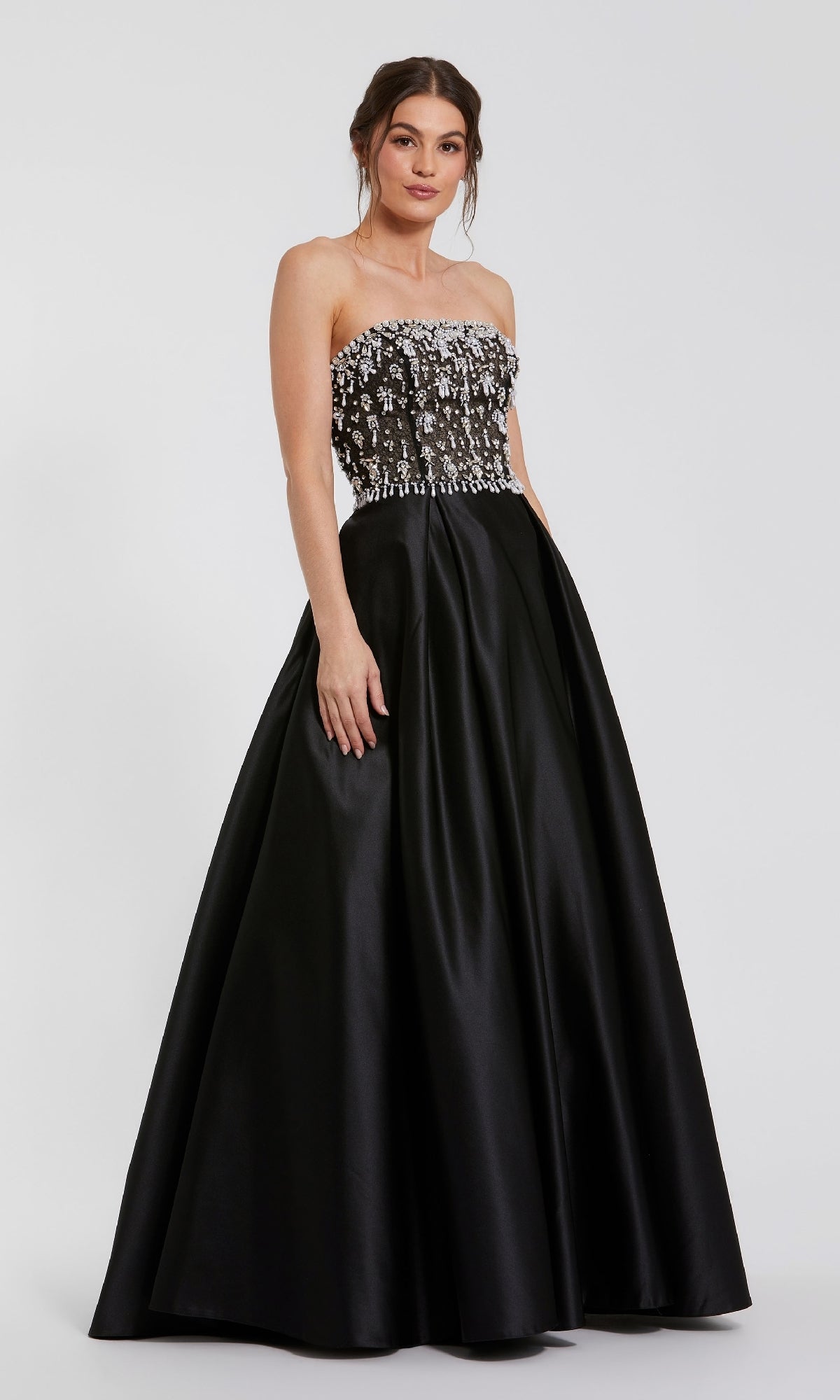 A woman models the Mac Duggal 2225 Strapless Black Satin Prom Gown, featuring a beaded floral-embellished bodice, standing against a plain white background.